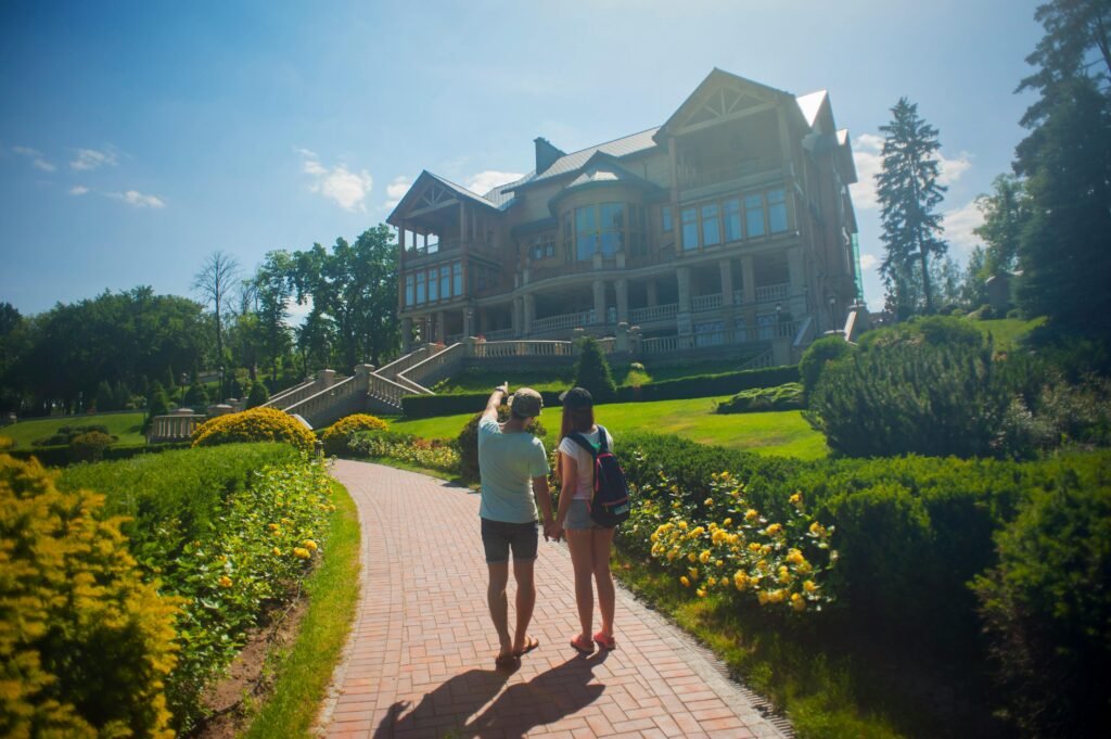 A young couple walks through a sunny garden path towards a large mansion. Scenic and serene.