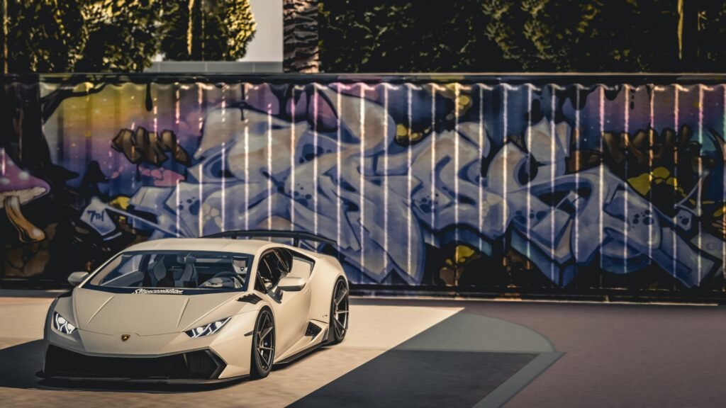 A sleek luxury sports car parked in front of a vibrant graffiti wall under bright daylight.