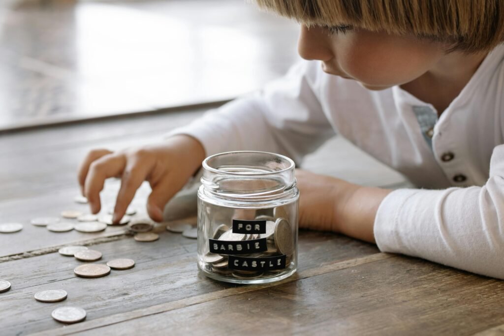 A young child collects coins in a jar labeled 'For Barbie Castle', symbolizing saving and dreams.